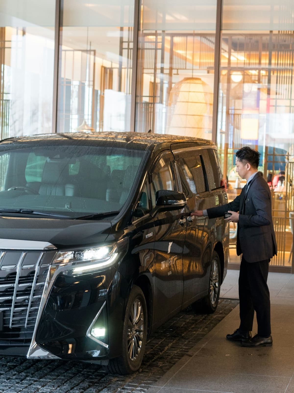 A chauffeur in a suit opening the door of a black executive people carrier